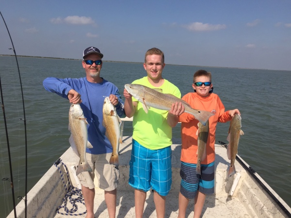 Father and sons holding redfish on boat